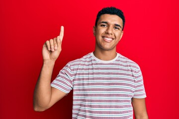 Naklejka premium Young arab man wearing casual clothes smiling with an idea or question pointing finger up with happy face, number one