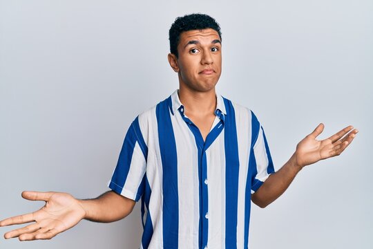Young arab man wearing casual clothes clueless and confused expression with arms and hands raised. doubt concept.