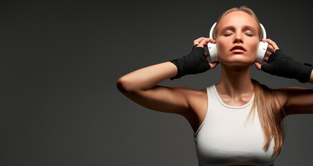 Beautiful slim girl listens to music through your wireless headphones before training in the gym. - obrazy, fototapety, plakaty