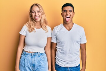 Young interracial couple wearing casual white tshirt sticking tongue out happy with funny expression. emotion concept.