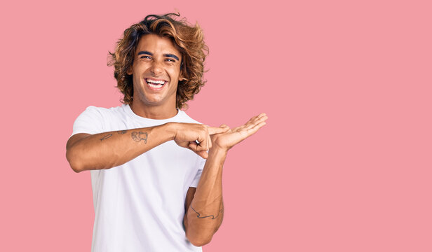 Young hispanic man wearing casual white tshirt amazed and smiling to the camera while presenting with hand and pointing with finger.