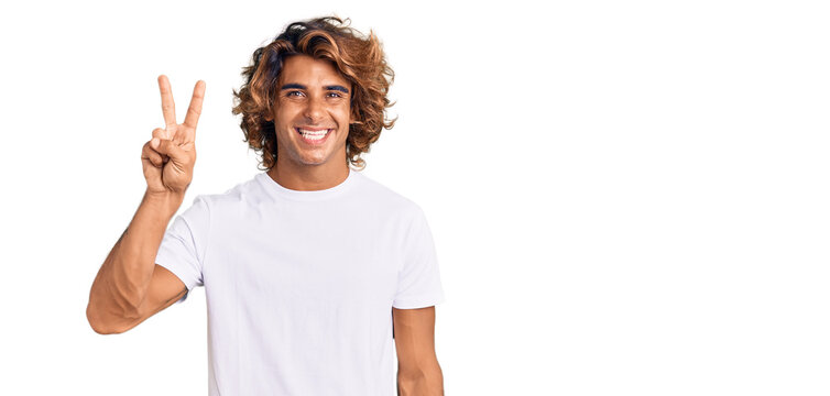 Young hispanic man wearing casual white tshirt showing and pointing up with fingers number two while smiling confident and happy.