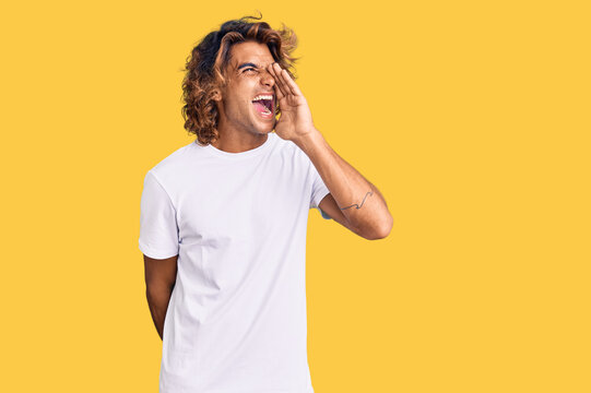 Young hispanic man wearing casual white tshirt shouting and screaming loud to side with hand on mouth. communication concept.