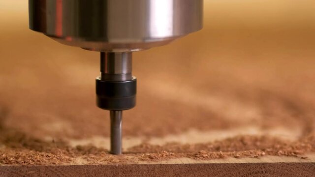 The head of the CNC machine cuts out a wooden decorative thing. The camera follows her. Splinters fly in different directions. extreme close-up