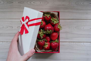 person opening gift box full of delicious fresh strawberries that are on a beige wooden table