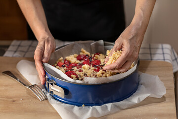 Hands putting crumble dough on a uncooked pie.