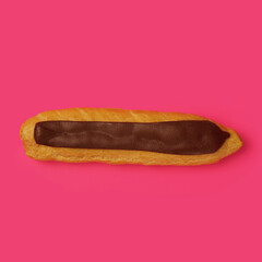 Eclair with custard and chocolate icing on a pink background, close-up. Traditional French dessert. homemade baking