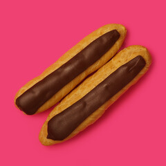 Two eclairs with custard and chocolate icing on a pink background. Traditional French dessert. homemade baking