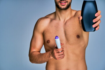 Fototapeta premium Guy with smile with a beard offers one of shampoo bottles. Beauty concept