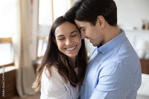 Tender Feelings Happy Caring Millennial Spouses Or Couple In Love Hugging In Living Room With Warmth And Affection Closing Eyes And Smiling Holding One Another In Arms Enjoying Sweet Moments Together Wall