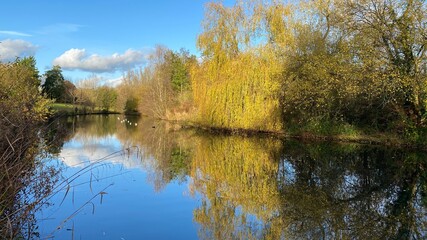 Fototapeta na wymiar Park canal in a beautiful sunny autumn day with trees and cloud reflecting on the calm, still water, scenic nature landscape, beautiful nature, blue sky and water.