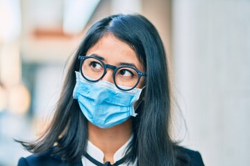 Young hispanic businesswoman wearing medical mask standing at the city.