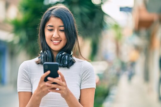 Young hispanic woman smiling happy using smartphone and headphones at the city.