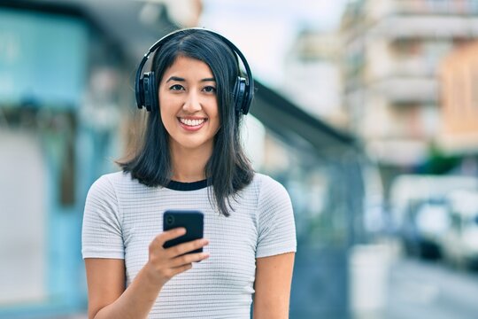Young hispanic woman smiling happy using smartphone and headphones at the city.