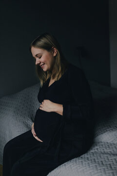 Pregnant woman sitting on bed, Sweden