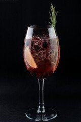 Refreshing wine cocktail with rosemary in a wine glass close up on black background