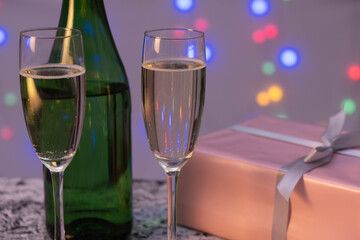 a bottle of champagne, two full glasses of champagne and a gift are on the table