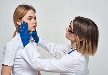 Woman doctor in a medical gown and in blue gloves with a stethoscope around her neck and a female patient 