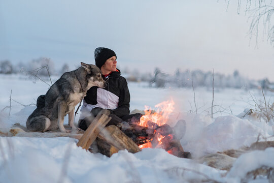 Woman with dog sitting at camp fire, Sweden