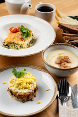 Lunch for a business lunch in a restaurant: lasagna, salad and cream soup, wooden table, high angle