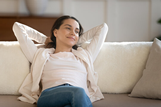 Enjoying serene moment. Successful satisfied millennial woman resting on comfy sofa at home looking aside with dreamy smile imagining pleasant things creating new plans visualizing future vacation