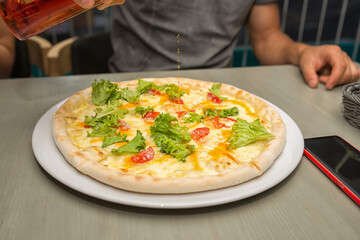 Man pours oil on the pizza, focus on lettuce shallow depth of field. The oil is poured on a vegetarian pizza with lettuce and slices of tomato.