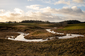Overflowing river forms a bend in a rural landscape. Patches of sunlight shines on the scene with...