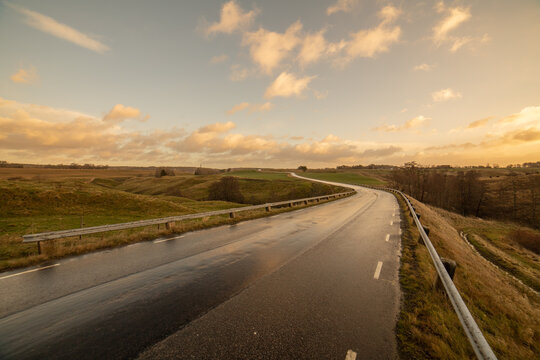 Winding road in a rural rolling hill landscape with side light from the morning sun. Nice clouds at the horizon