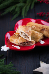 Christmas or New year snack. Pancake stuffed with meat on red festive tree plate with green pine tree branches. Family celebration food, home made crepes with filling.