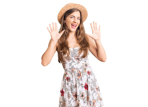 Beautiful caucasian young woman wearing summer hat showing and pointing up with fingers number ten while smiling confident and happy.