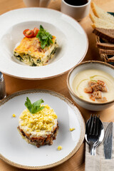 Lunch for a business lunch in a restaurant: lasagna, salad and cream soup, wooden table, high angle