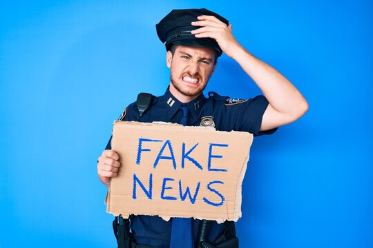 Young caucasian man wearing police uniform holding fake news banner stressed and frustrated with hand on head, surprised and angry face