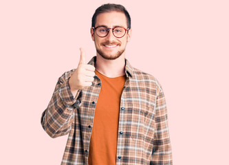 Young handsome caucasian man wearing casual clothes and glasses smiling happy and positive, thumb up doing excellent and approval sign