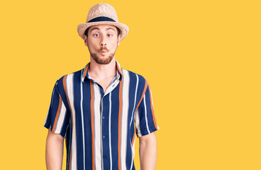 Young handsome caucasian man wearing summer hat making fish face with lips, crazy and comical gesture. funny expression.