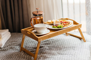 morning breakfast on a tray in bed. Omelet, tea, sausages, lettuce, croutons with butter