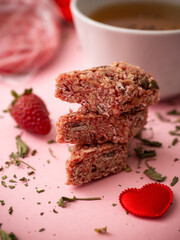 Healthy sweet dessert snack and breakfast. Cereal granola bar with nuts and strawberries and cup tea on a light pink background.