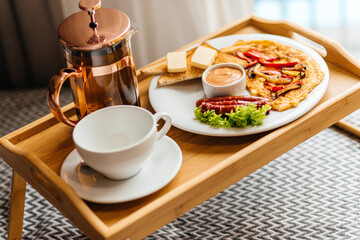 morning breakfast on a tray in bed. Omelet, tea, sausages, lettuce, croutons with butter