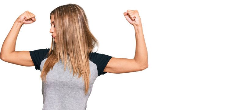 Young blonde woman wearing casual clothes showing arms muscles smiling proud. fitness concept.