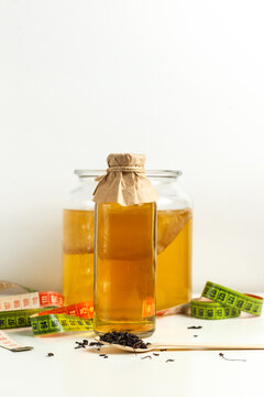 Kombucha Drink In A Glass Bottle, A Can Of Kombucha Mushroom, Tea Leaves On A Wooden Spoon And Measuring Tape On A Light Background