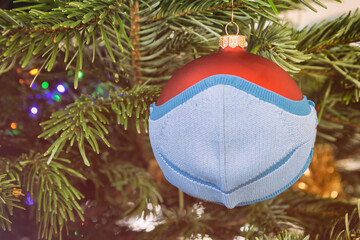 Isolated Christmas decoration ball wearing textile children face mask. COVID-19 holidays safety concept.