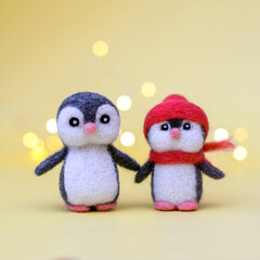 Two woolly toy penguins on a yellow background with bokeh