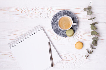 Composition from an empty diary with a spring, a cup of coffee and macaroons and a branch of eucalyptus on a white shabby wooden table. Fashion flat lay