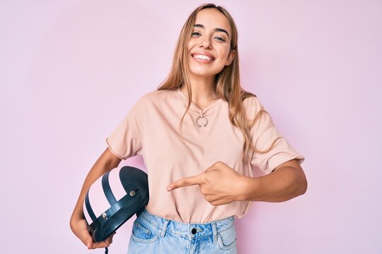 Young beautiful blonde woman holding motorcycle helmet smiling happy pointing with hand and finger