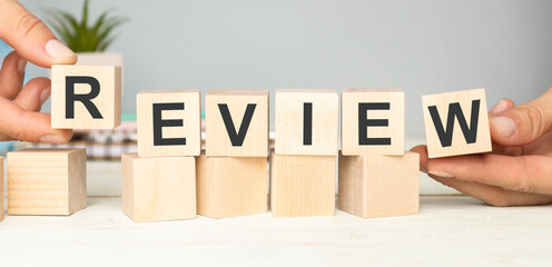 Word REVIEW written on wooden cubes. Pen and paper and cubes on blue table