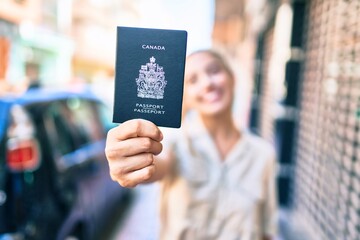 Young beautiful blonde caucasian woman smiling happy outdoors on a sunny day showing Canada passport