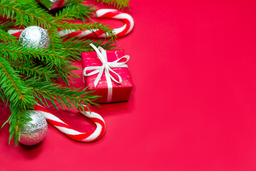 Close-up of branches of christmas tree decorated with gift boxes, christmas balls and candy canes on red background with copy space.