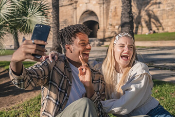 black man with blonde girl sitting on the grass having a lifestyle taking a selfie
