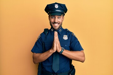 Handsome hispanic man wearing police uniform praying with hands together asking for forgiveness...