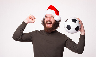 Cheerful bearded hipster man screaming and celebrating victory and holding soccer ball, santa claus