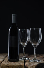 Dark bottle of red wine and empty glasses on rustic wooden table on black background. Advertising and promotion concept. Space for text. Tasty alcoholic drink.